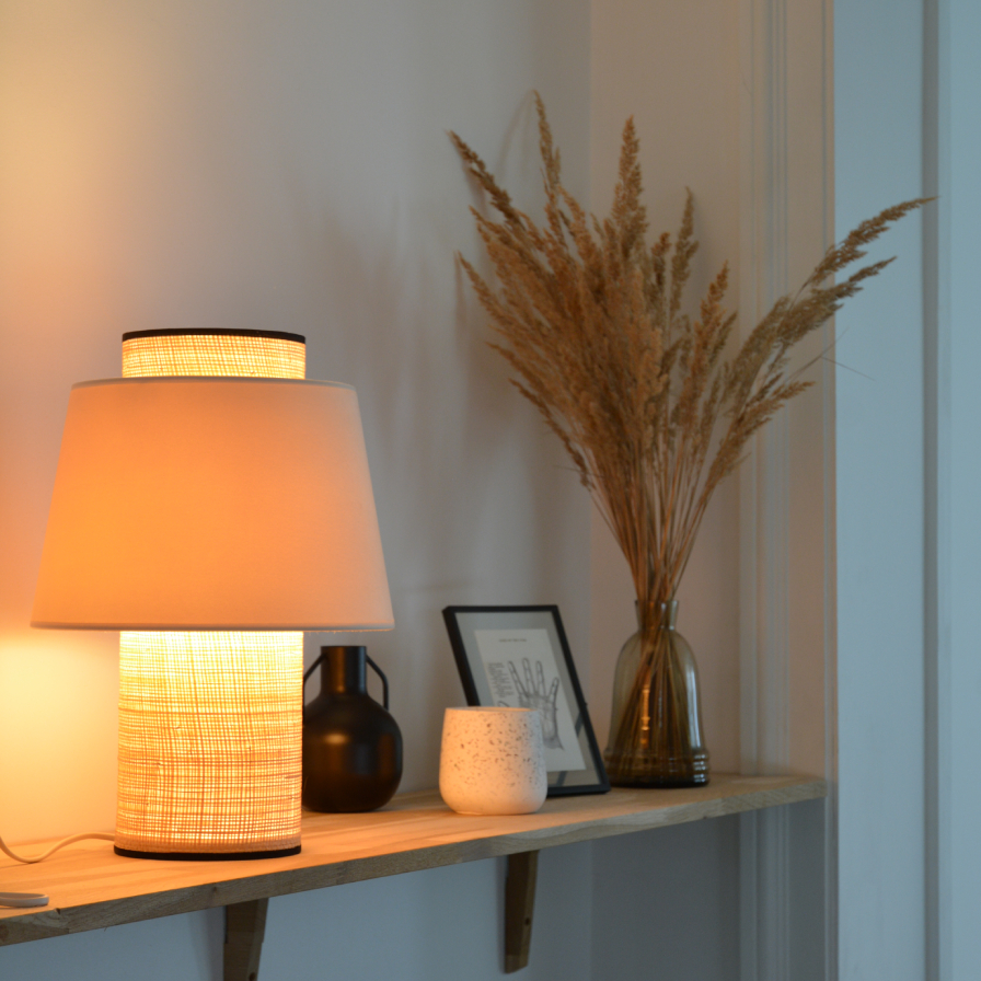 La lampe LULEA allumée effet lumineux chaleureux projeté par le velours et le rotin, créant une ambiance naturelle.