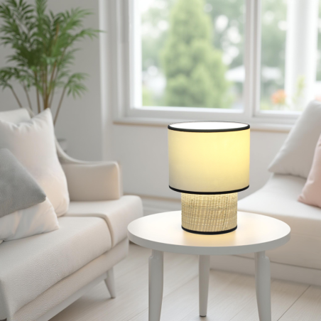 Lampe à poser en velours écru, beige et rotin naturel sur une petite table de salon. Intérieur blanc épurée et moderne.